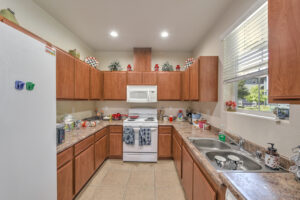 Community Kitchen, tile floor, white appliances, dual stainless steel sink, brown cabinetry, window above sink.