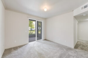 Interior Unit Living Room, Sliding Glass patio door, Neutral toned wall paint and carpeting, overhead light fixture.