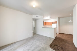 Interior Unit Living Room, Breakfast attached to kitchen, hanging light fixture in dining area, wood like floors in dining area, neutral toned wall paint and carpeting in living room.