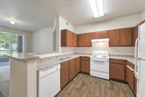 Interior Unit Kitchen, Wood-like floors, white appliances, dual stainless steel sink, light brown cabinetry, laminate countertops.