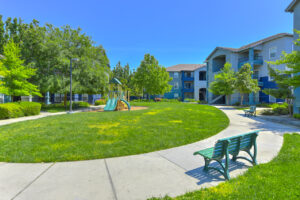 Exterior Playground, benches along sidewalks, residential buildings around playground area, soft ground in playground, grass field.