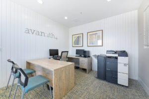 Interior Leasing office, contemporary carpeting with yellow and blue accents, avanath signage above rust desk, xerox printer, contemporary art on the walls, white walls.