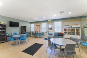Interior Childrens Center, tables for activities, tv on wall, toy cubbies, childrens art on walls, tile floor.
